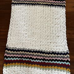 a white crocheted blanket with multicolored stripes on it sitting on top of a wooden floor