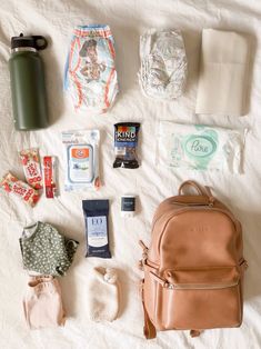 the contents of a diaper bag laid out on top of a white bed sheet