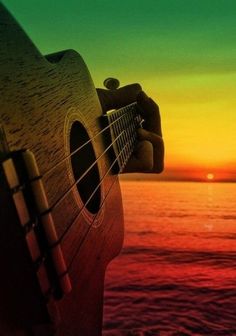 the sun is setting over the ocean with an acoustic guitar in front of it's body