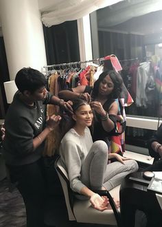 a woman getting her hair styled by two other women in front of a clothing rack