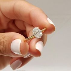 a woman's hand holding a ring with a diamond on it and the middle finger