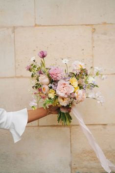 a person holding a bouquet of flowers in front of a brick wall with white ribbon