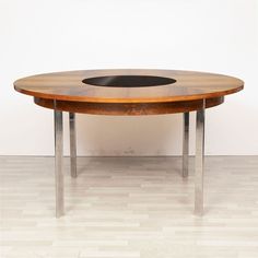 an oval wooden table with metal legs and a black center piece in the middle on a hard wood floor