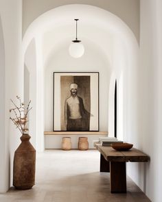 a large painting hangs on the wall next to a wooden bench and vase with flowers in it