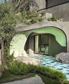 an outdoor room with green walls and plants on the roof, surrounded by large rocks