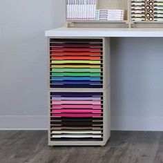 a white desk with many different colored papers on it and a wooden shelf holding several file folders