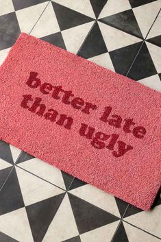 a red door mat that says better late than ugly on the floor next to a black and white checkered floor