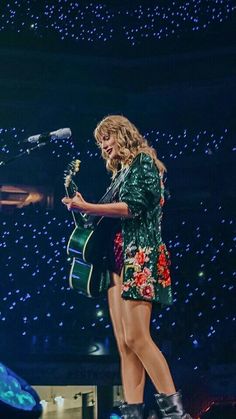 a woman standing on top of a stage holding a guitar