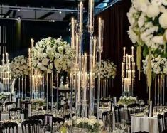 the tables are set up with white flowers and candles in tall vases on them