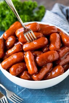 a white bowl filled with hot dogs on top of a blue cloth next to silverware