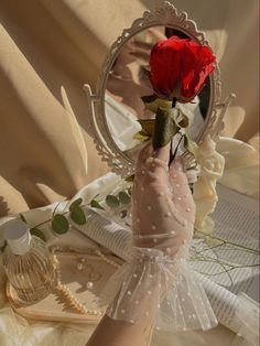 a person holding a red rose in front of a mirror on top of a bed