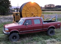 a red pick up truck parked next to a large yellow machine in a field with grass