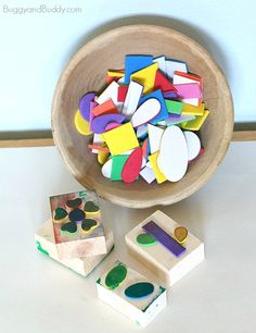 a wooden bowl filled with lots of different colored shapes next to two blocks of wood