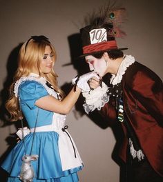 two people dressed up as alice and the mad hatter, one is pointing something at the other