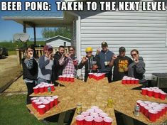 a group of people standing around a wooden table with cups on it and one person holding up a beer