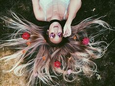 a woman laying on the ground with her hair blowing in the wind and flowers all around her