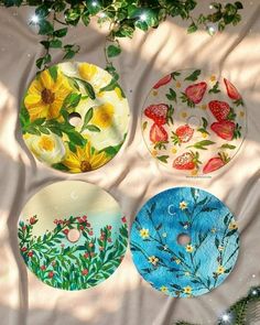 four glass plates with flowers and leaves painted on them sitting next to a christmas tree