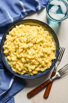 a bowl filled with macaroni and cheese on top of a table next to two forks