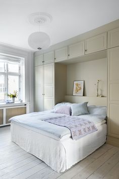 a large white bed sitting in a bedroom next to a tall wooden dresser and window