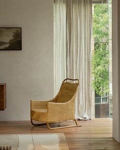 a wicker rocking chair sitting in front of a sliding glass door with white curtains