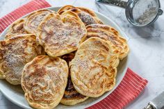 a white plate topped with pancakes covered in powdered sugar on top of a red towel