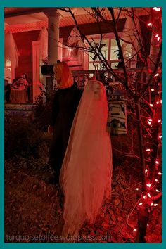 two people dressed up in halloween costumes standing next to a tree with red lights on it