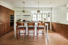 a kitchen with wooden cabinets and white counter tops, along with bar stools that match the hardwood flooring