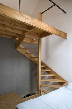 a bed sitting under a wooden staircase next to a wall