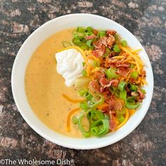 a white bowl filled with soup topped with sour cream and green onions, cheese and bacon