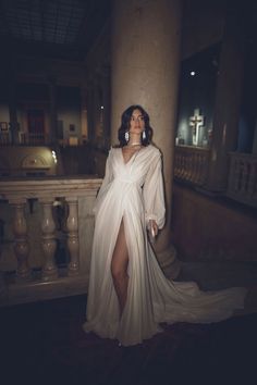 a woman in a white dress standing next to a pillar with her legs spread out