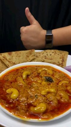 a white plate topped with a bowl of soup next to pita bread and a hand giving the thumbs up sign