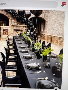 a long table set up with black plates and silverware for an outdoor dinner party