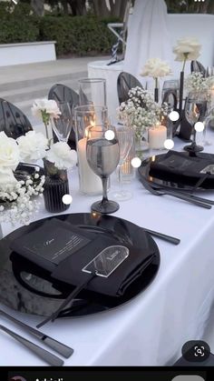 the table is set with black plates, silverware and white flower centerpieces