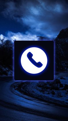 an illuminated phone sign on the side of a road in front of a dark sky