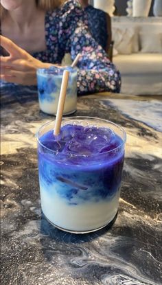 two people sitting at a table with drinks in front of them, one is blue and the other is white