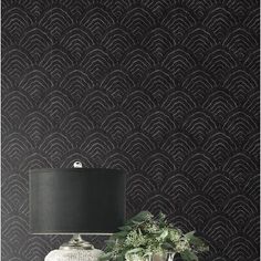 a lamp on a table next to a vase with flowers in it and a black wallpaper