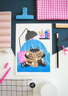 there is a black cat reading a book on the table next to some crafting supplies