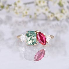 three different colored stones in gold ring on white surface with flowers and petals behind them