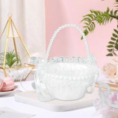 a white basket sitting on top of a table next to pink flowers and other decorations