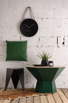 a clock mounted to the side of a white brick wall next to a green table