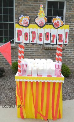 an orange and yellow popcorn cart on the side of a building with red and white striped flags