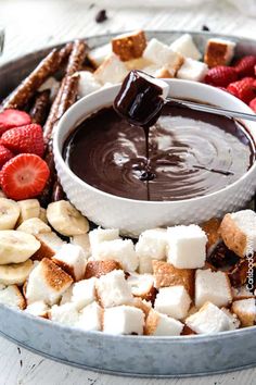 a bowl filled with marshmallows, strawberries, and chocolate sauce being drizzled over