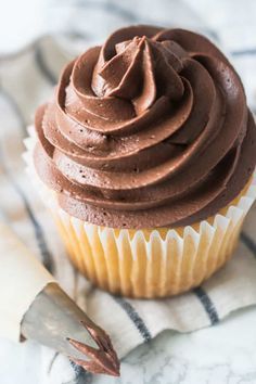 a cupcake with chocolate frosting sitting on top of a napkin next to a knife