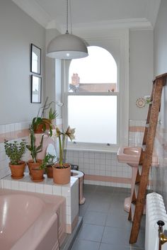 a bathroom with pink tiles and potted plants on the window sill, next to a ladder