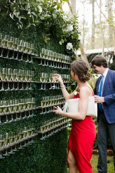 a man and woman standing next to each other in front of a green wall filled with glasses