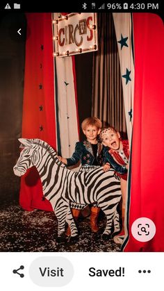 two children are sitting on a fake zebra in front of circus sign with stars and stripes