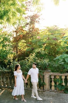 a man and woman holding hands while standing next to each other in front of trees