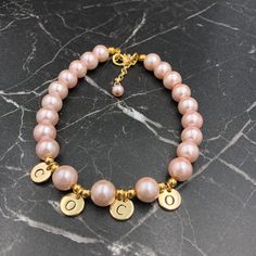 a pink pearl bracelet with gold charms on a black marble surface and the letter c