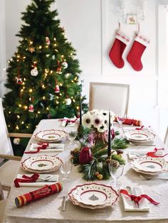 a table set for christmas dinner with stockings hanging on the wall and tree in the background