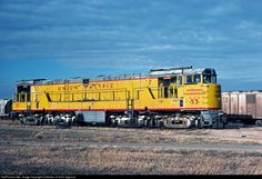 a yellow and red train traveling down tracks next to dry grass on a cloudy day